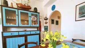A dining area with a wooden table, chairs, and a blue tablecloth. There is a vase with yellow flowers on the table.