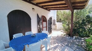 An outdoor patio with a round table covered in blue polka dot tablecloth, surrounded by white plastic chairs.