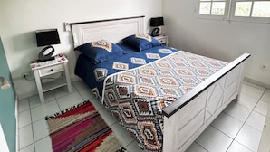 A bedroom with a bed, a ceiling fan, a window, and a wall-mounted air conditioner. - VILLA C'MARGOT - 110 M2 (MARIGOT)