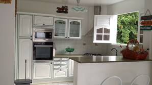 A kitchen with white cabinets, a microwave, a sink, and a window with a view of greenery. - VILLA C'MARGOT - 110 M2 (MARIGOT)