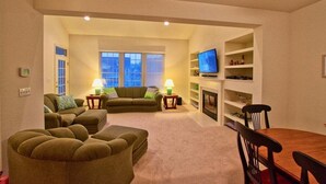 A living room with a sofa set, a TV, a fireplace, and a dining table. - Bear Trap Dunes * 3BR Golf Villa (Ocean View)