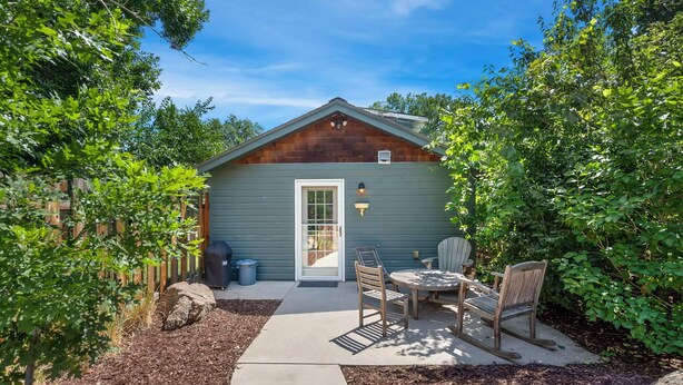 A small wooden cabin with a door, a window, and a patio area with a table and chairs.