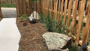 A garden area with a wooden fence, mulch, rocks, and plants.