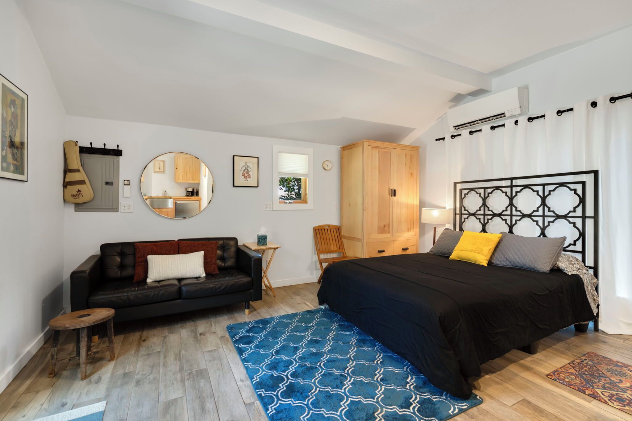 Une chambre à coucher avec un lit, un canapé en cuir noir, une petite table en bois, un miroir et une armoire.
