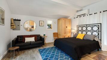 Une chambre à coucher avec un lit, un canapé en cuir noir, une petite table en bois, un miroir et une armoire.