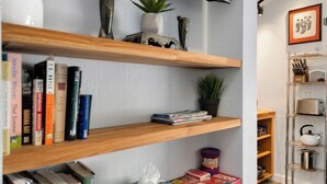 A room with wooden shelves holding books, a plant, and a box of Yahtzee dice.
