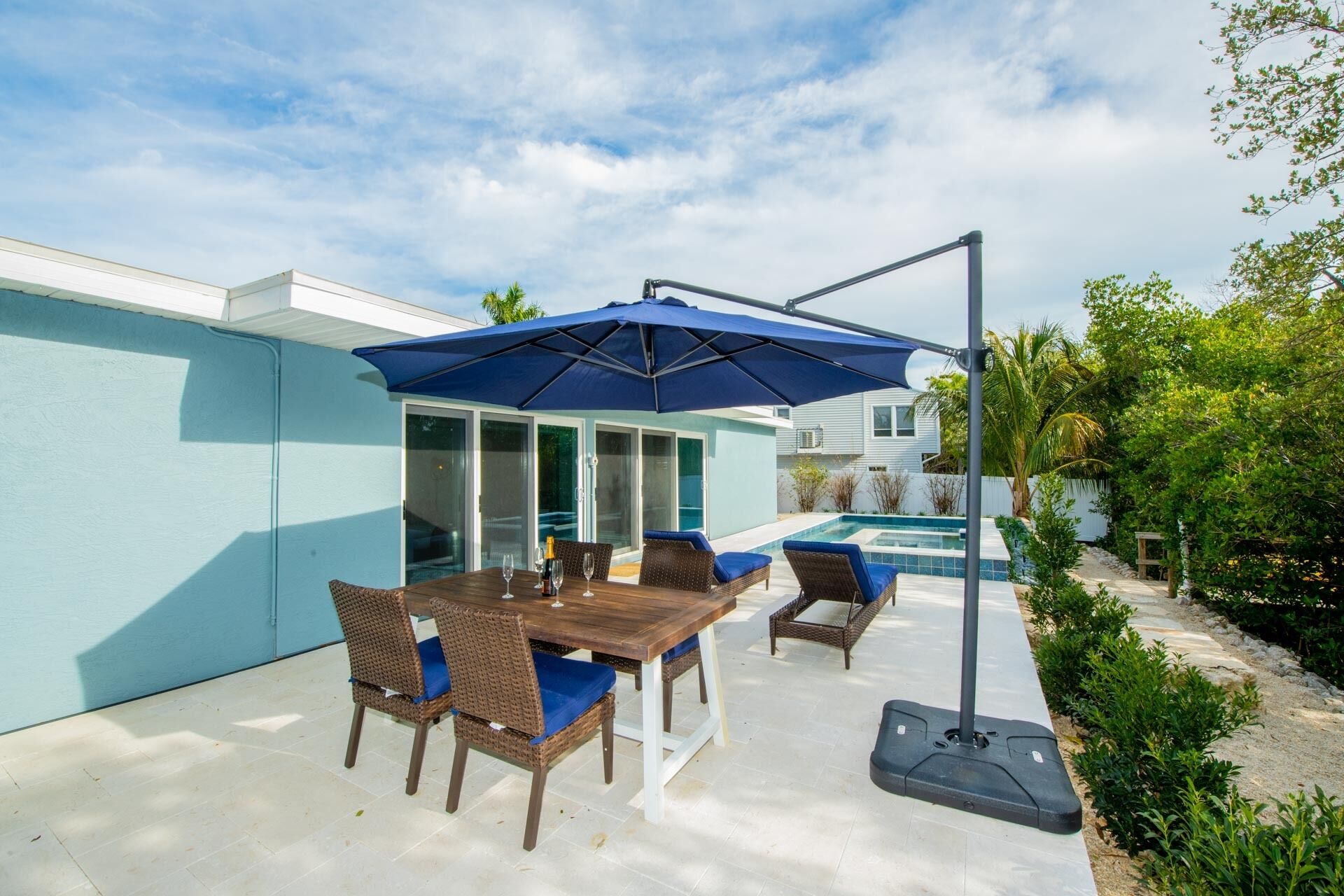 An outdoor patio with a pool, a table with chairs, and a blue umbrella.