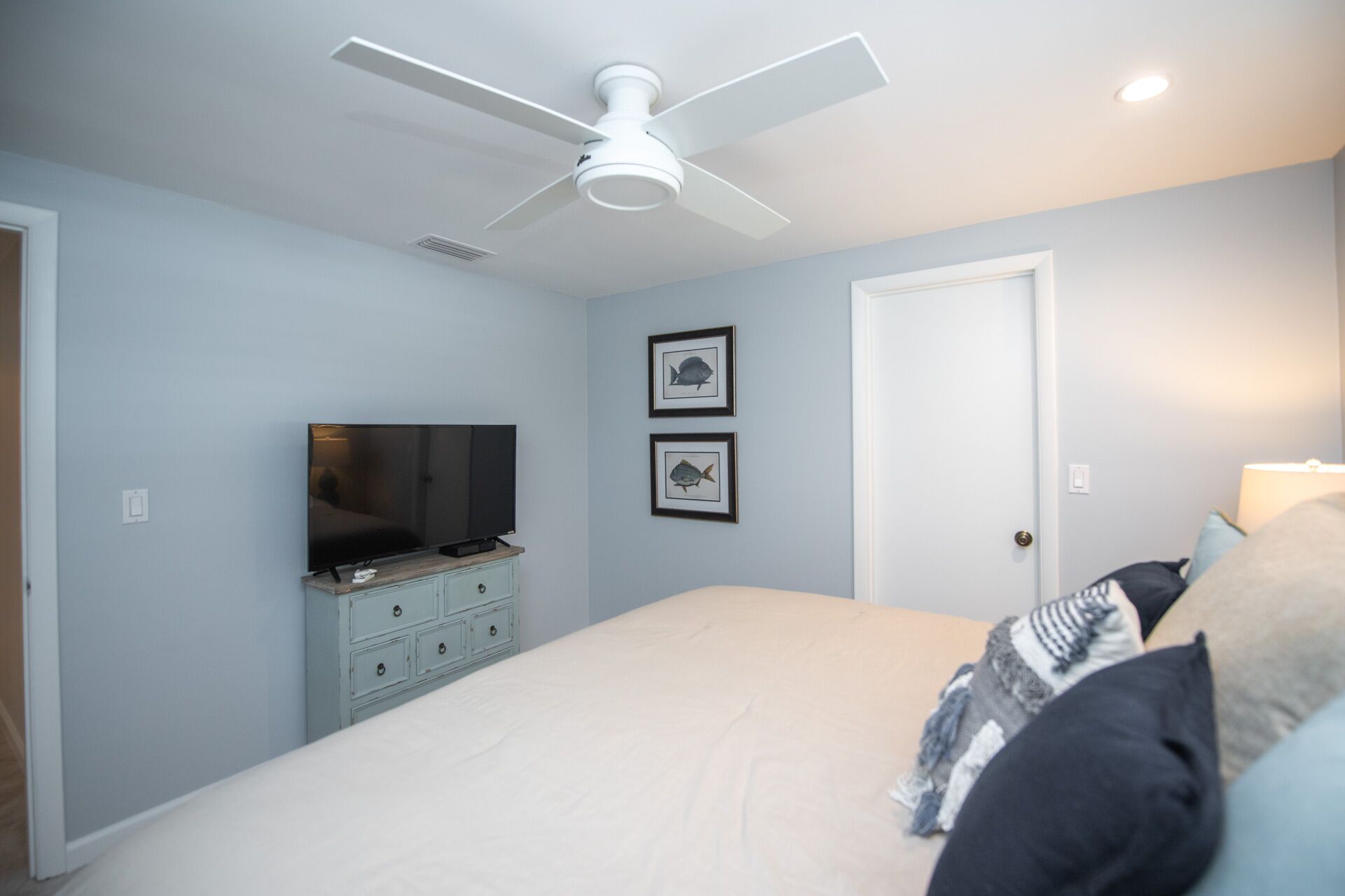 Ein Schlafzimmer mit einem Bett, einem Fernseher auf einer Kommode, einem Deckenventilator und zwei gerahmten Bildern an der Wand.