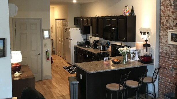 Una cocina moderna con armarios oscuros, una isla central con taburetes altos, un refrigerador y un microondas.