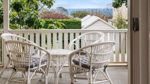 Un espace extérieur aménagé avec des meubles en osier blanc, comprenant une table et des chaises, offrant une vue sur un jardin et la mer.