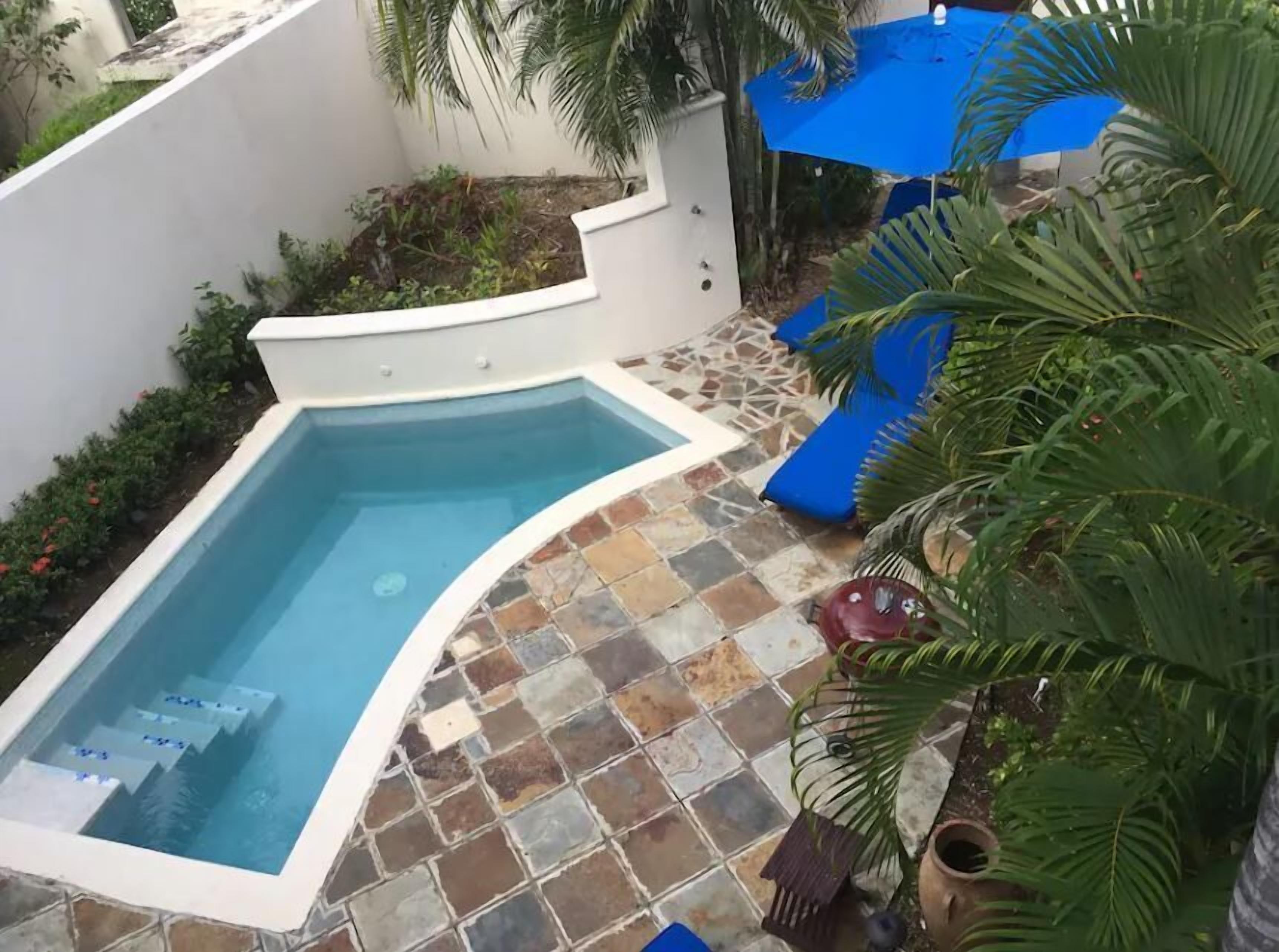 A swimming pool with a curved edge, surrounded by a tiled deck and a white wall.
