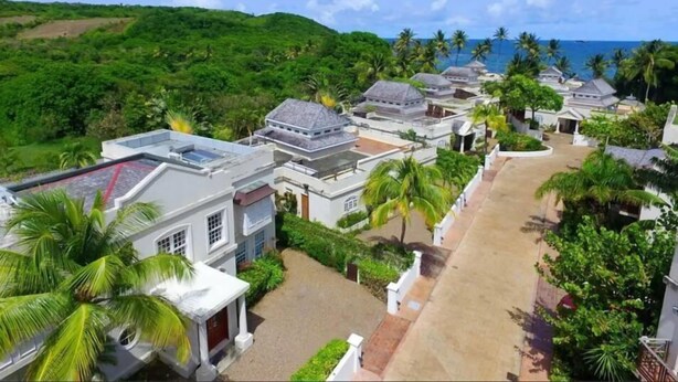 A resort with multiple bungalow-style buildings, a central paved area, and a backdrop of lush greenery and the ocean. - Cotton Bay Townhouse (Gros Islet)