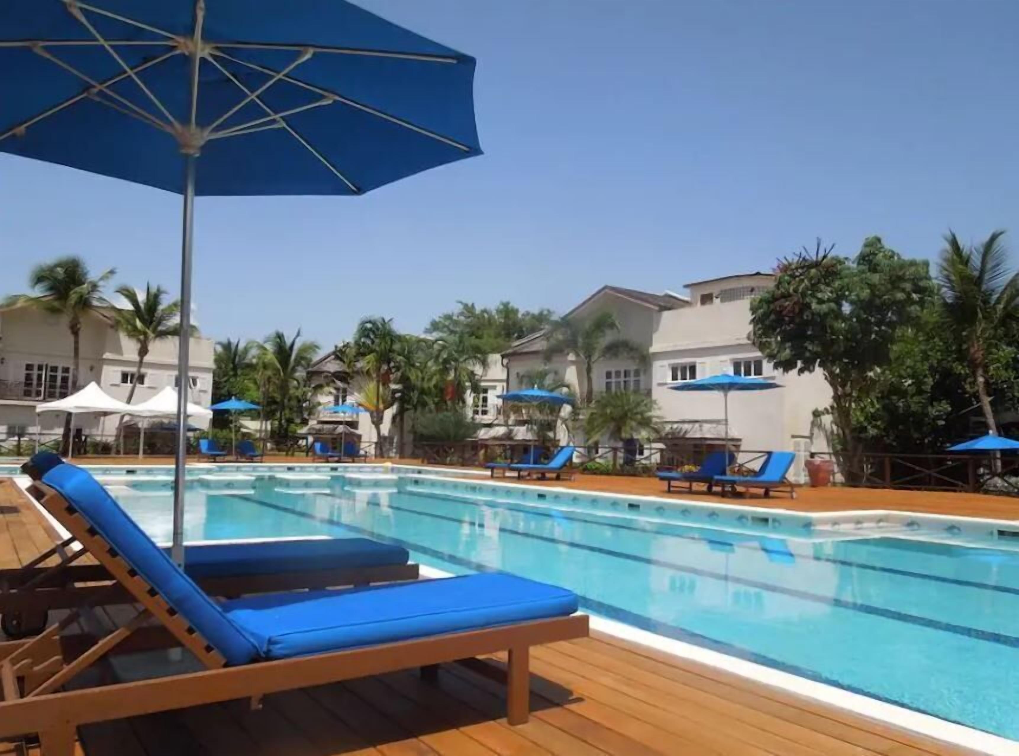 A pool area with lounge chairs and umbrellas, surrounded by palm trees and buildings.