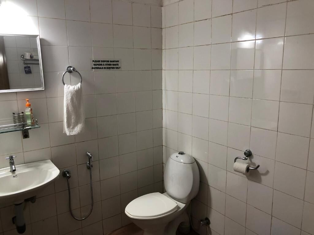 Un baño pequeño y limpio con inodoro, lavabo y ducha. Un letrero indica desechar tampones y otros residuos en contenedores especiales.