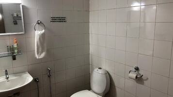 Un baño pequeño y limpio con inodoro, lavabo y ducha. Un letrero indica desechar tampones y otros residuos en contenedores especiales.