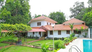 Una casa de dos pisos con piscina, rodeada de abundante vegetación y un césped cuidado.