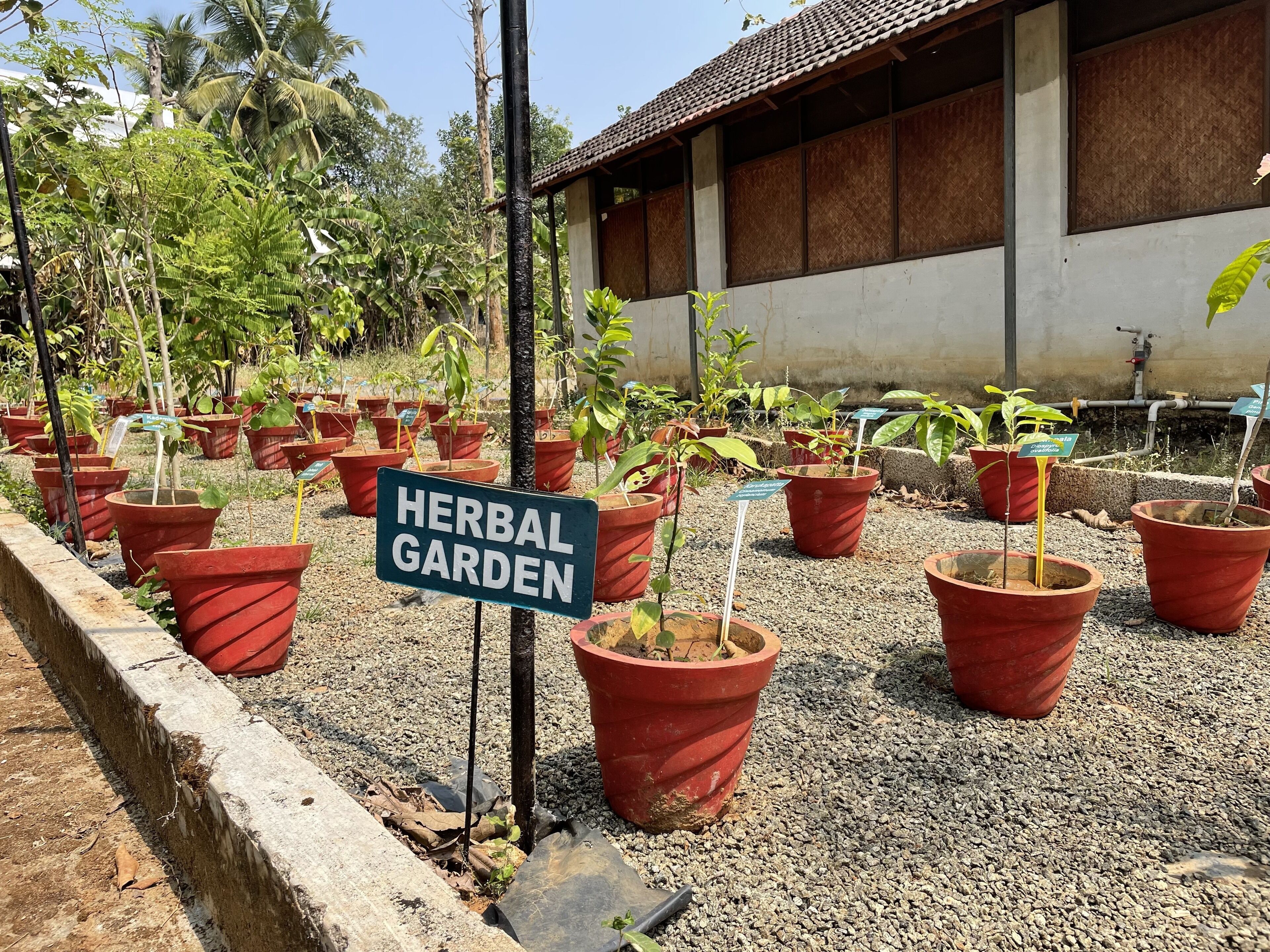 Un letrero que dice "HERBAL GARDEN" frente a un edificio con techo de tejas y base de concreto.