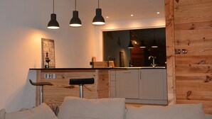 A modern kitchen with a wooden accent wall, a built-in bench, and pendant lighting. - Boutique Alpine Chalet with Panoramic Views next to Ski Lift (Thollon-Les-Mémises)