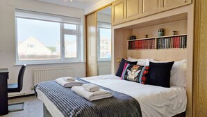 Une chambre à coucher avec un lit, un bureau, une chaise, une fenêtre et une bibliothèque.