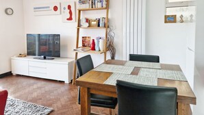 Un salon moderne avec une table à manger en bois, des chaises noires, un meuble de rangement blanc avec un téléviseur à écran plat et une bibliothèque contenant divers objets.