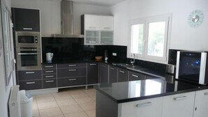 A modern kitchen with dark cabinetry, a large island, stainless steel appliances, and a window providing natural light. - Casa del Erizo: Moraira. (Moraira)