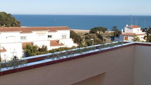 Un quartier résidentiel en bord de mer, avec des bâtiments blancs et des toits recouverts de tuiles rouges, une plage et une vue dégagée sur la mer.