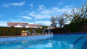 Une piscine avec des chaises longues, un ciel bleu dégagé et des bâtiments en arrière-plan.