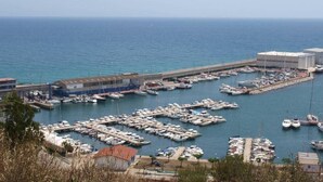 Un port de plaisance où sont amarrés de nombreux bateaux, un grand bâtiment sur la droite et une vue dégagée sur la mer.