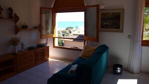 Un salon avec vue sur la mer, un canapé de couleur turquoise, des meubles en bois et un tableau accroché au mur.