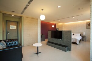 Una habitación de hotel moderna con televisión de pantalla plana, un sofá, una mesa redonda y una cama con ropa blanca.