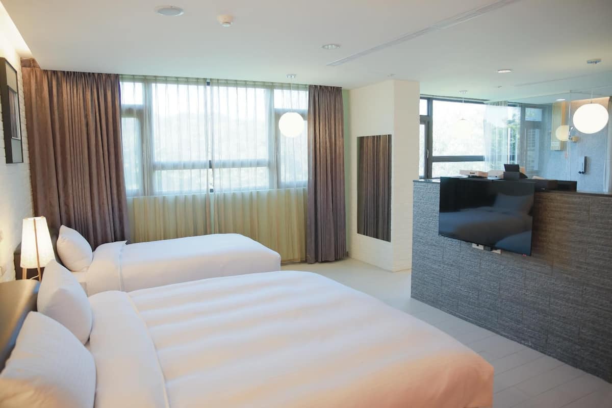 Ein Hotelzimmer mit zwei Betten, einem Schlafsofa, einem Fernseher und großen Fenstern mit Vorhängen.