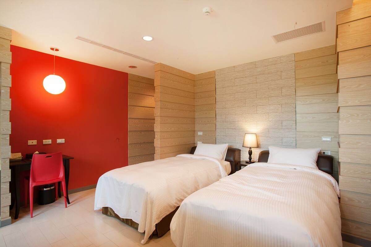 Ein Hotelzimmer mit zwei Betten, einem Schreibtisch mit Stuhl und einer roten Akzentwand.