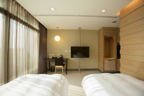 Habitación de hotel con dos camas, un escritorio, televisor y zona de ducha.