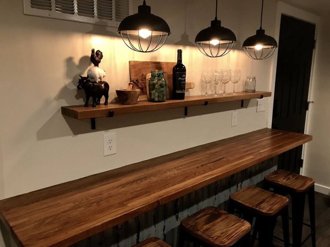 A kitchen with a long wooden countertop, three bar stools, and pendant lights.