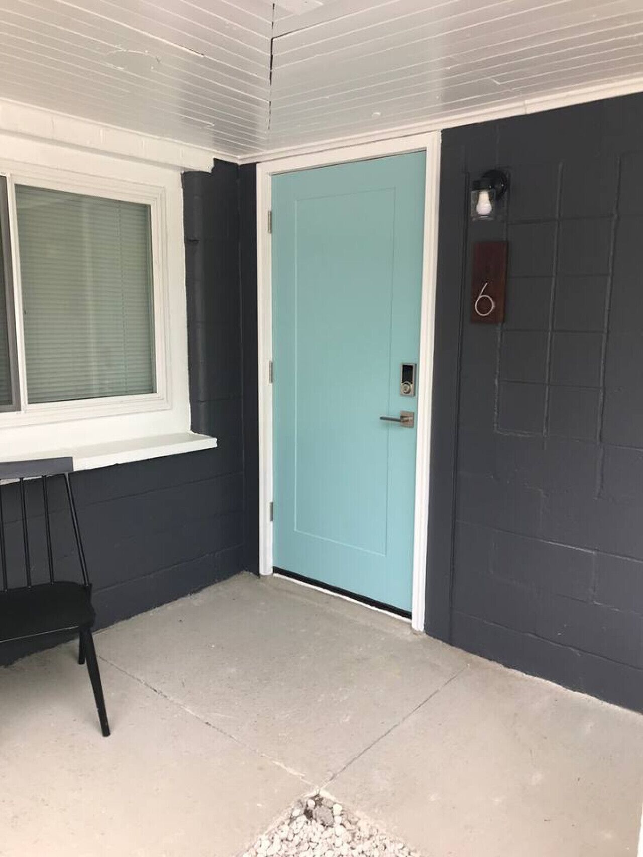 A corner of a room with a teal door, a window with blinds, and a black chair.