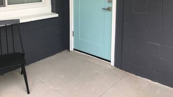 A corner of a room with a teal door, a window with blinds, and a black chair.