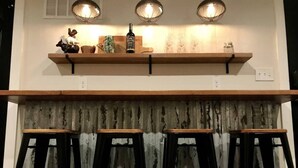 Une cuisine avec trois tabourets en bois, une étagère en bois ornée d’objets décoratifs et un rideau au motif vieilli.