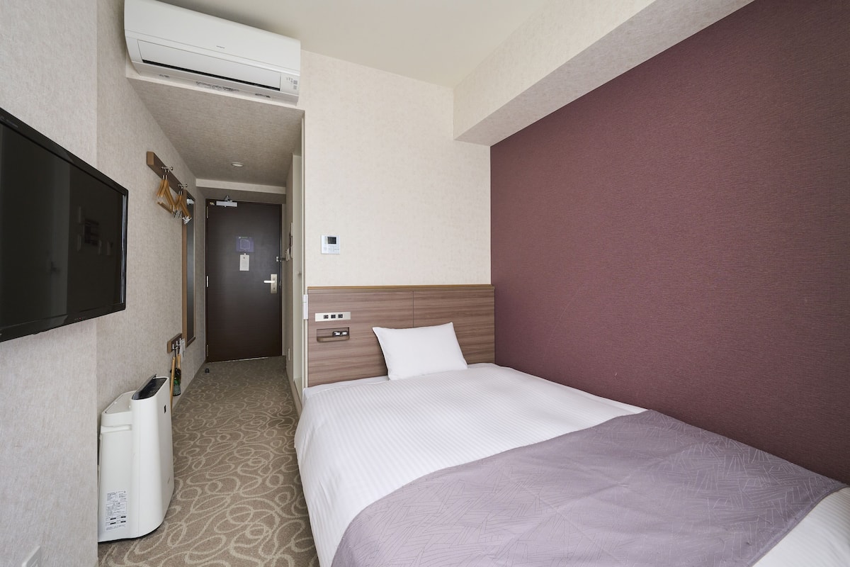 A hotel room with a large bed, a TV mounted on the wall, a minibar, and a door leading to a hallway.