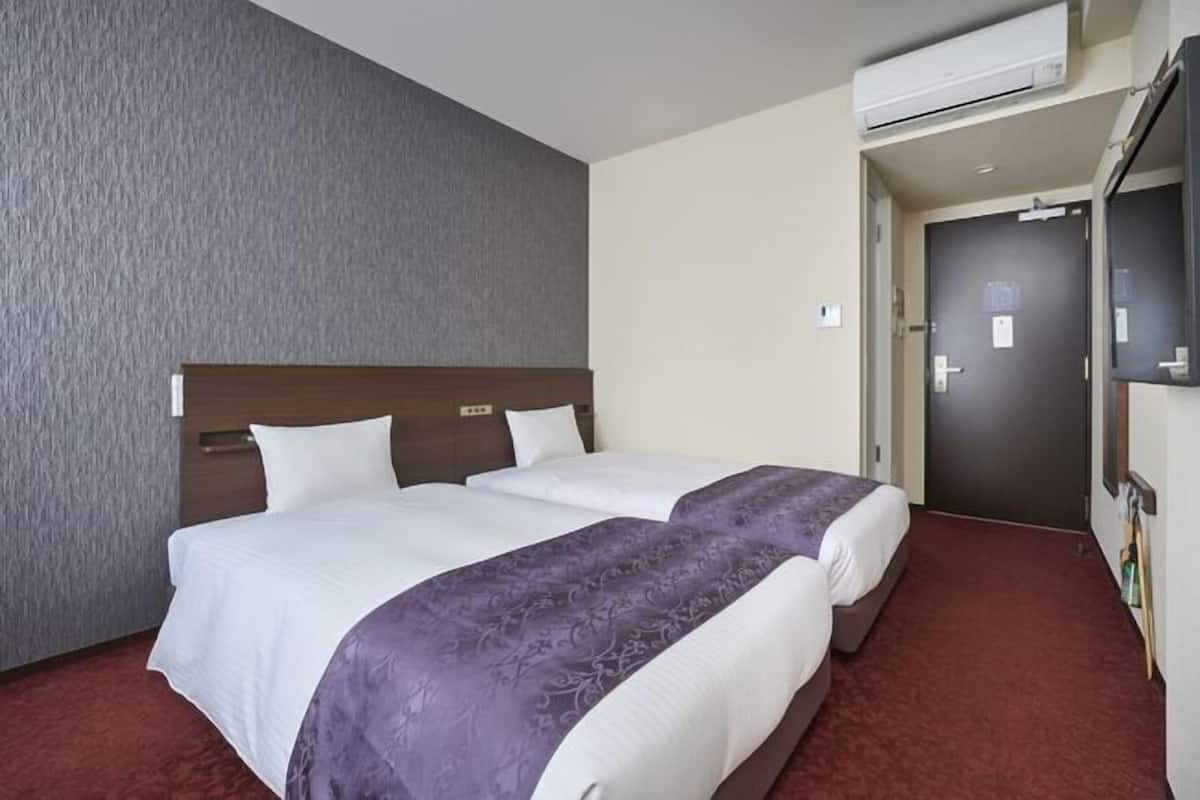 A hotel room with two beds, a grey textured wall, a red carpet, and an air conditioning unit.