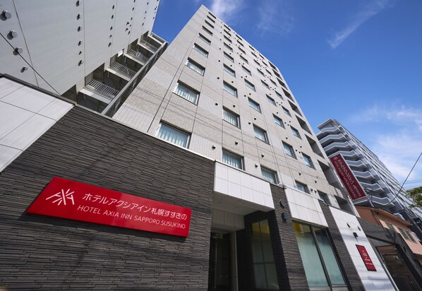 Um edifício moderno de hotel com uma placa vermelha destacada indicando ser o Hotel Axia Inn.