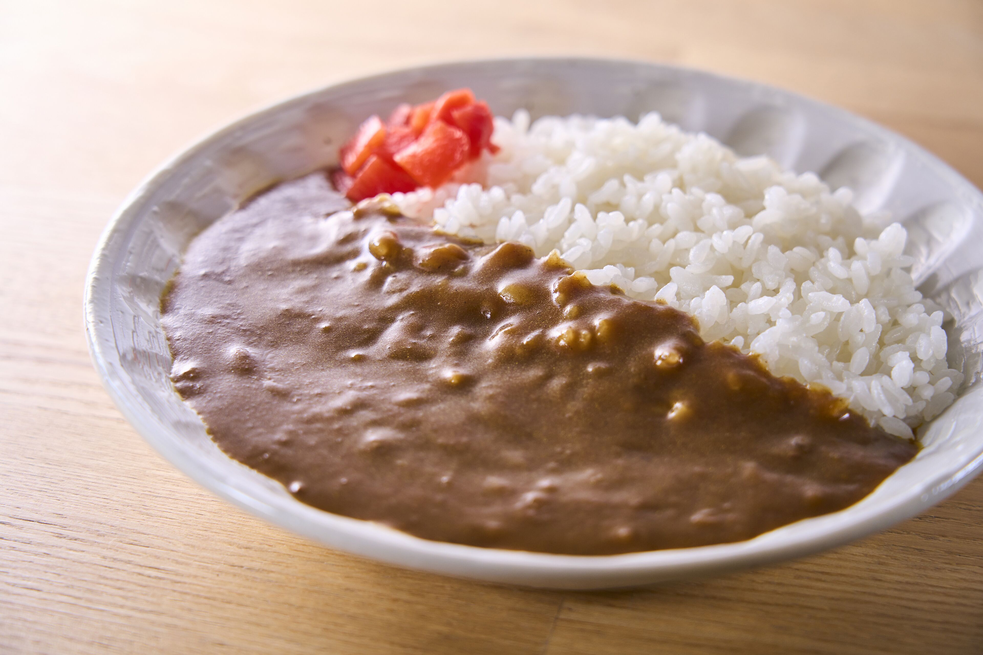 A plate with white rice, brown sauce, and a piece of red fruit.