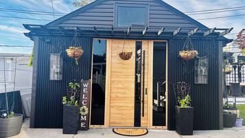 Een klein, donker gebouw met een uitnodigend bord, een houten deur en hangende plantenbakken.