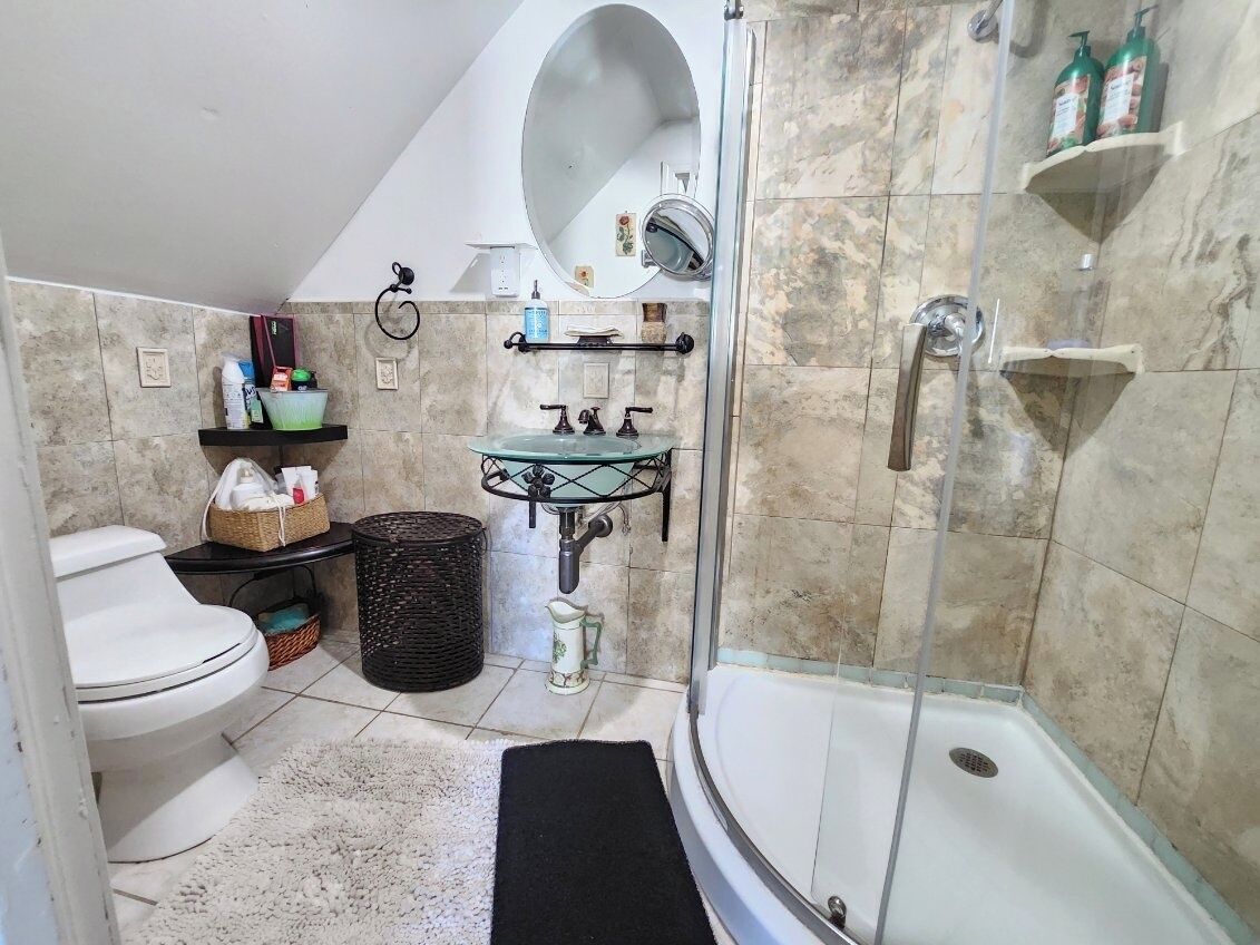 A bathroom with a toilet, sink, shower, and a mirror.