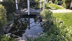 Un jardín con un estanque, un puente de madera y abundante vegetación.