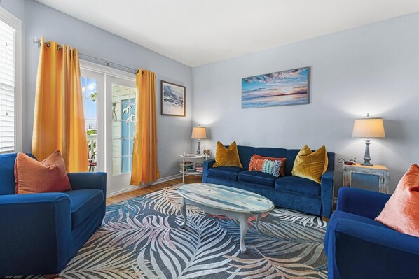 A living room with two blue sofas, a patterned rug, and a painting on the wall. - 2Bed2Bath, sleeps 6. Pet friendly. Pool. Hot tub. walking distance to the beach. (Corpus Christi)