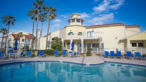 A pool area with lounge chairs and umbrellas, a building with a balcony, and palm trees. - 2Bed2Bath, sleeps 6. Pet friendly. Pool. Hot tub. walking distance to the beach. (Corpus Christi)