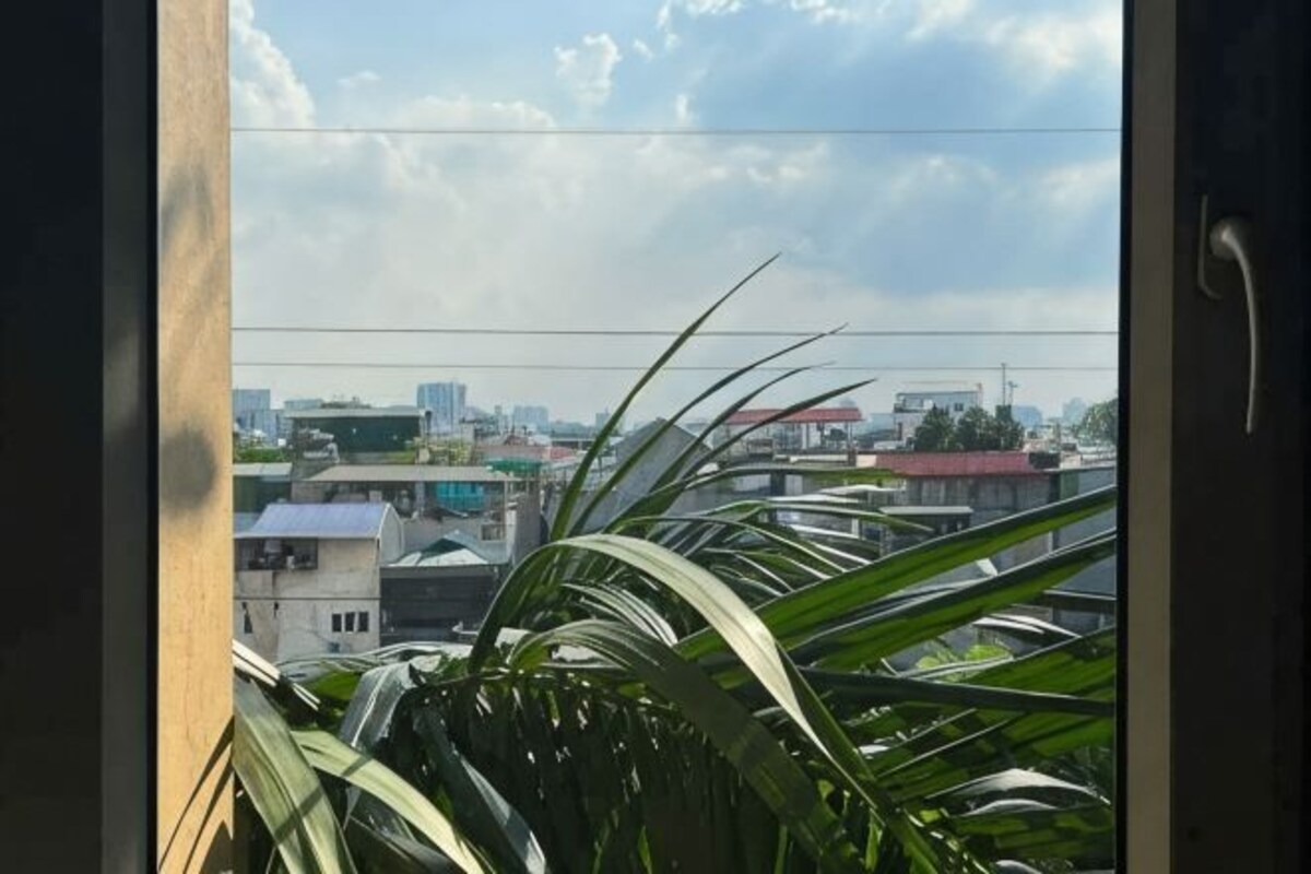 Une vue à travers une fenêtre, avec un paysage urbain en arrière-plan, comprenant des bâtiments et un ciel dégagé.