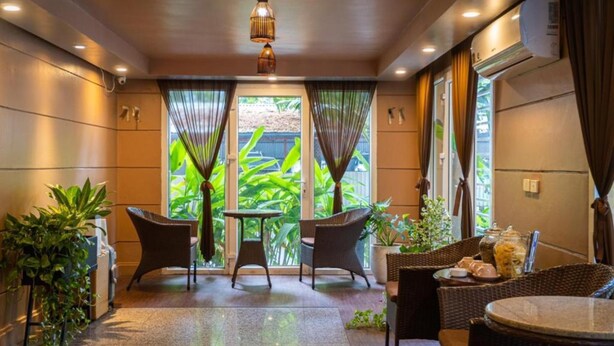 A cozy indoor seating area with wicker furniture, a small table, and potted plants. - Ha Noi Le Grand Hotel (Hanoi)