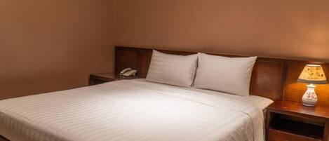 A neatly made bed with white linens, a wooden headboard, a bedside table with a lamp, and a phone.