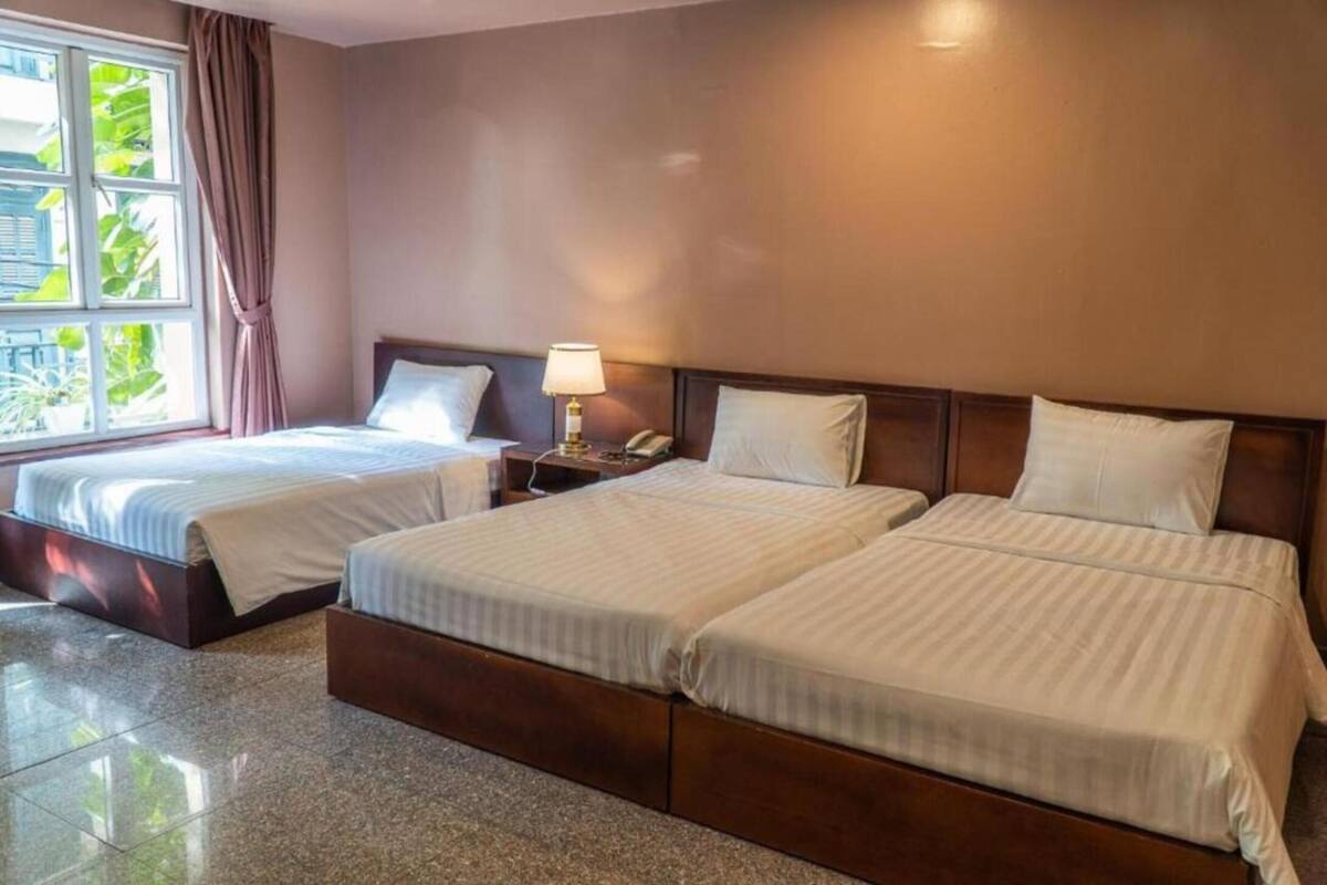 A hotel room with two beds, a nightstand with a lamp, and a window with curtains.